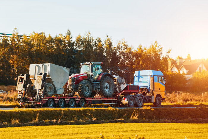 A heavy truck with a flatbed trailer transports a big tractor used for farming and agriculture.