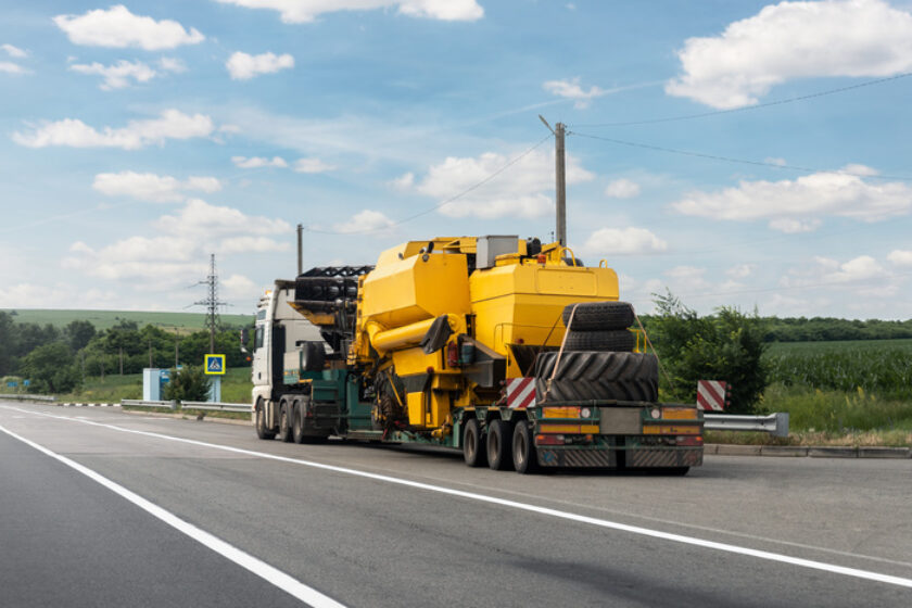 Long heavy industrial truck with semi trailer platform transport disassembled combine harvester machine on common highway on bright summer day. Agricultural equipment transportation service