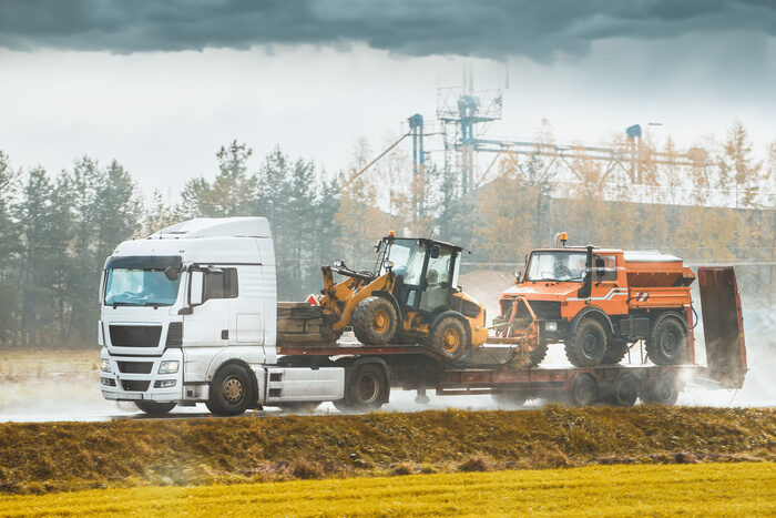 Farm Equipment Haulers - A white truck hauls heavy construction equipment on a trailer. Loaders and bulldozers are transported by a white truck